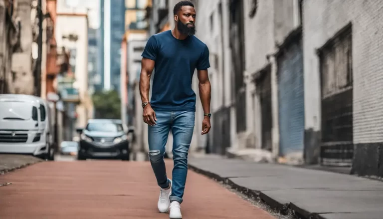 Homem estiloso usando pochete preta de couro com camiseta branca e calça jeans em uma rua urbana, edifícios modernos ao fundo, dia ensolarado.